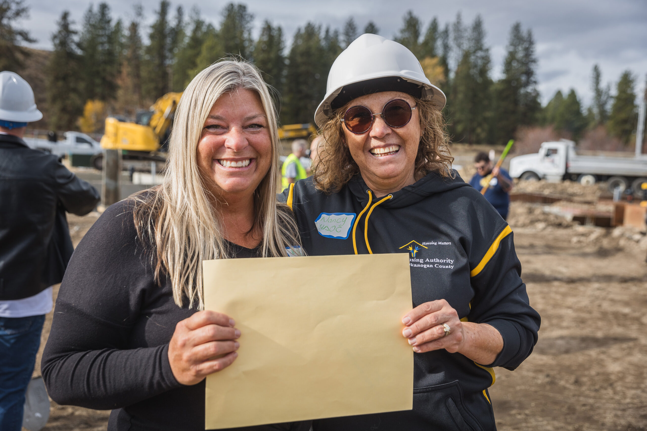 (L) Beth Stipe, CFNCW Executive Director and (R) Nancy Nash-Méndez, HAOC Executive Director, hold the ARC loan repayment check during the groundbreaking for the Wildrose Multifamily Affordable Housing project in Winthrop, WA.