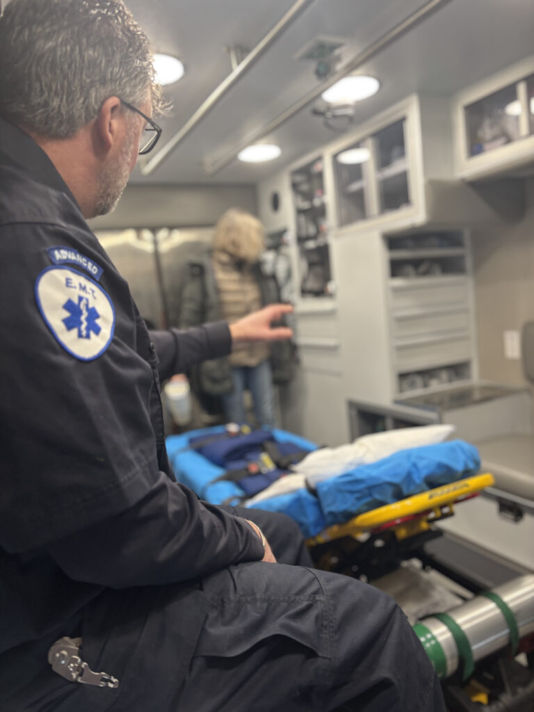 An EMT seated inside an ambulance next to a stretcher and medical equipment.